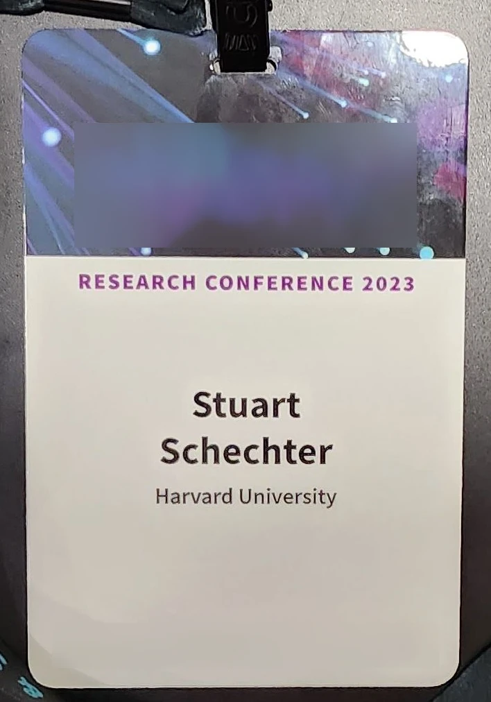 A name tag with the conference logo taking up the top half, then the author's first name (Stuart) on one small line, the family name on the next line (Schechter), and institution (Harvard) on the third line. At the bottom is another branding logo.