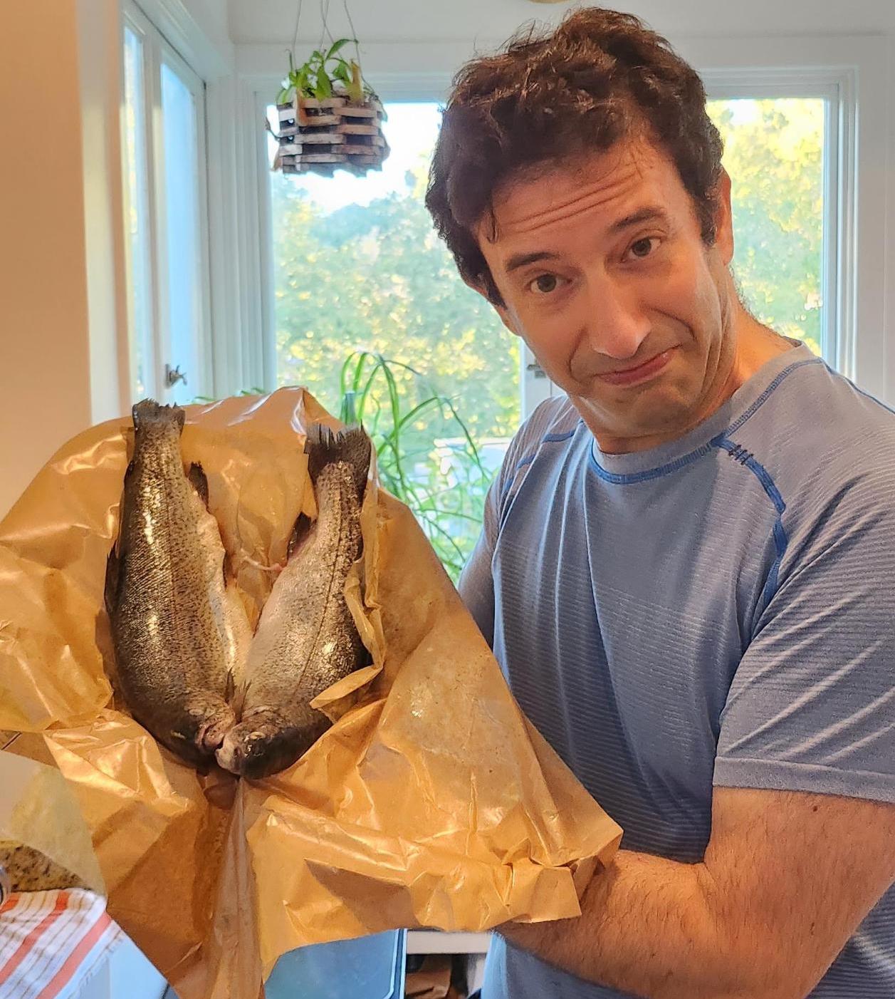 The author holding two trout in their paper grocery wrapping.